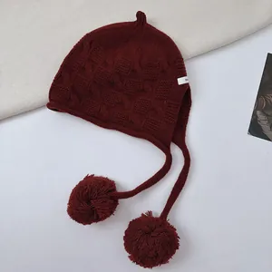 Detailed view of premium burgundy wool knit elf hat with earflaps and large pom-poms
