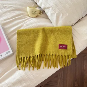Detailansicht eines senfgelben Wollschals mit Fransen auf einem Bett