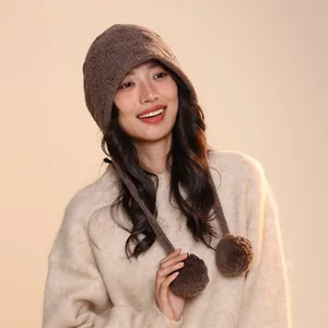 Detailed view of a brown wool knit hoodie beanie with pom-pom accents on an Asian model