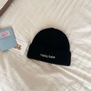 Close-up detail of a soft black knitted beanie hat with 'Hello Kele' embroidery texture