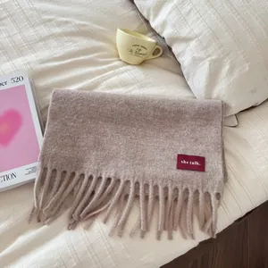 Detailansicht eines weichen beigen Wollschals mit eleganten Fransen und einem roten Webeetikett