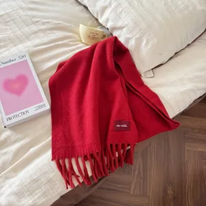Detailansicht eines dicken roten Wollschals mit weichen Quasten auf Bett