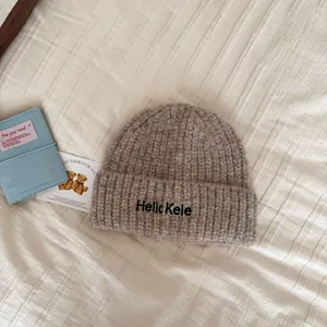 Close-up of a soft beige knitted beanie hat with embroidered text on white textured cloth