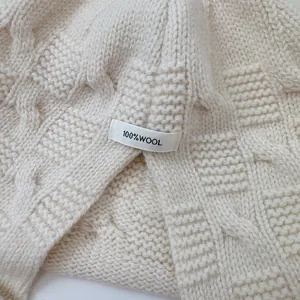 Close-up of 100% wool tag on white knitted elf pumpkin cloak beanie.