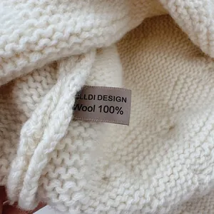 Detailed macro view showing 100% wool composition label on a soft cream knitted hat.