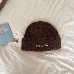 Detail view of a cozy brown knitted beanie with Hello Kele embroidery on cream fabric