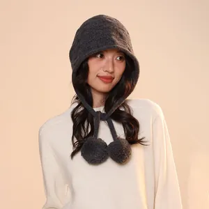Close-up detail of a dark grey wool pumpkin-style knit hat with decorative hanging pom-poms
