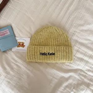 Detail shot of a yellow knitted winter beanie with black embroidery text.