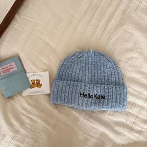 Close-up of light blue knitted beanie with "Hello Kele" embroidery on a soft background.