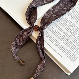 Detail der braunen Vintage-Seidenschal-Halskette mit Paisley-Muster auf einem Buch