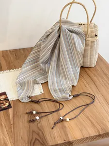 Detail of vintage striped triangular scarf with beaded drawstring on a wooden table.