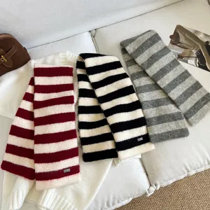 Detail of three striped wool neck warmer scarves in red, black, and grey on a white sofa