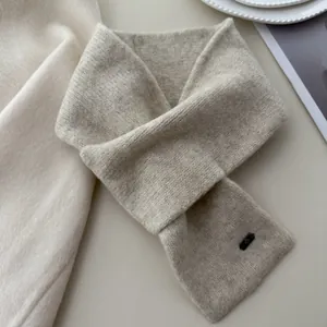 Macro detail of a soft beige knitted cross neck warmer scarf with a small metal logo