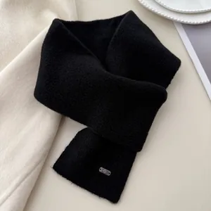 Close-up detail of a soft black knitted cross scarf featuring a minimalist metal tag