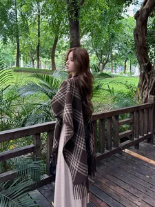 Elegante bruine en beige geruite sjaal-poncho met franjes op een vrouwelijk model buiten