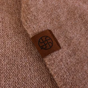 Close-up detail of a camel wool blend knit shawl featuring a decorative brand patch