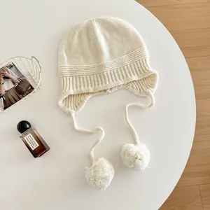 Close-up detail of a minimalist 100% wool knitted balaclava with soft white pom-poms