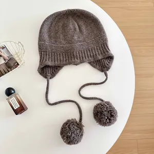 Detail view of a brown 100% wool knit balaclava hat featuring fluffy pom-poms