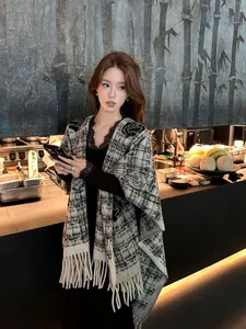 Elegante geruite poncho sjaal met franje kwastjes gedragen door model in stijlvolle setting.