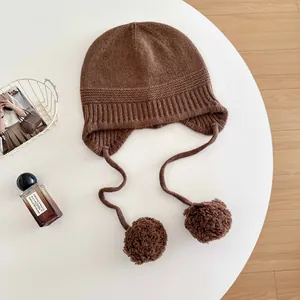 Detailed shot of a brown 100% wool knit balaclava hat featuring soft decorative pom-poms