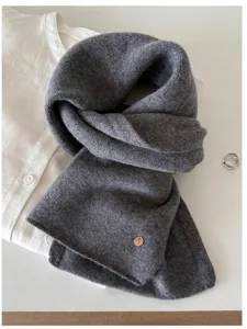 Detailed texture of a soft grey 100% wool knit scarf with a small vintage metal charm