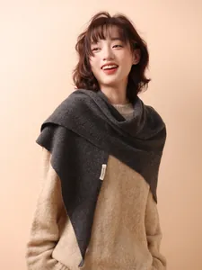 Detail view of a 100% wool dark grey knitted triangular shawl worn over a beige sweater