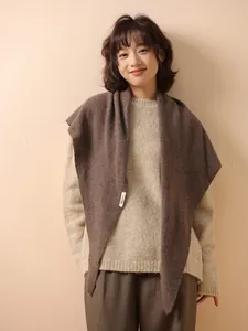 Close-up of a model wearing a brown 100% wool knitted triangular shawl in soft light