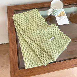 Primer plano de bufanda de punto verde suave con texturas de panal y trenzas