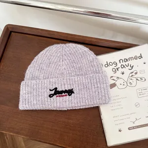 Detailansicht einer lila Strickmütze mit Journey-Bestickung auf einem Holztablett