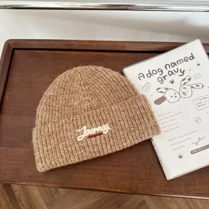 Detailansicht einer braunen Strickmütze mit weißem Journey-Schriftzug bestickt