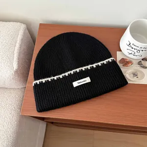 Dettaglio ravvicinato di un berretto nero in maglia con striscia bianca e toppa con logo Mulanduo