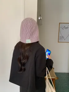 Back view of a woman wearing a lavender cable-knit trapper hat in a minimalist interior setting