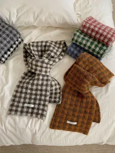 Variety of soft knit plaid scarves in autumn colors displayed on a cozy white bedsheet