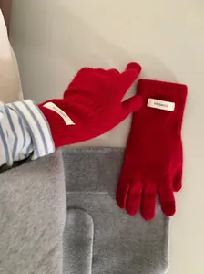 Detail view of red 100% merino wool knitted gloves showing the material composition label