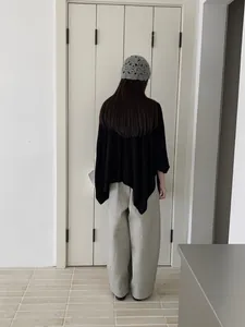 Vista posteriore di uno scialle asimmetrico nero con pantaloni grigi a gamba larga chic.