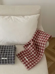 Lifestyle shot of red and grey checkered knitted scarves on a minimalist white sofa