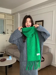 Model wearing a bright green wool scarf with fringe and a white label detail.
