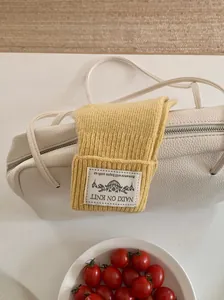 Close-up of yellow knitted arm warmer gloves with brand tag shown on a white leather bag