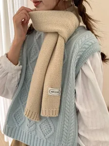 Detailopname van een beige gebreide sjaal met ARCL'SEE merklabel op een model.
