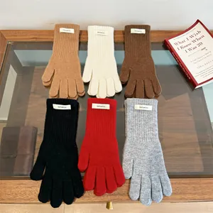 Detail view of 100% merino wool knit gloves in six colors on a wooden glass table.