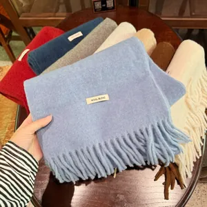Surtido de bufandas de mezcla de lana en colores lisos con flecos y etiquetas de material.