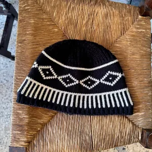 Vista dettagliata del berretto in lana lavorata a maglia Fair Isle bianco e nero su sedia.