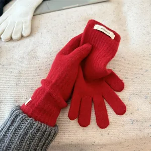 Close-up detail of red 100% merino wool knitted gloves showing soft texture and label