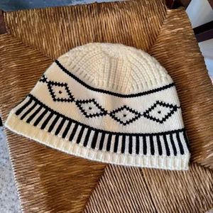 Dettaglio di un berretto in maglia crema con motivi a rombi neri in stile Fair Isle.