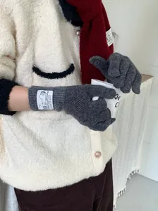 Détail de gants en laine tricotée rétro gris avec étiquette de marque esthétique.