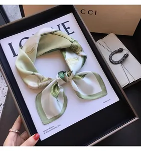 Elegant faux silk square scarf with green botanical leaf print displayed on magazine