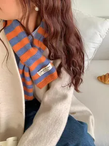 Close-up of orange and blue striped wool blend scarf worn with a white coat