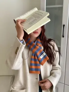 Model wearing a cozy pumpkin orange and blue striped wool blend cross-through knitted scarf