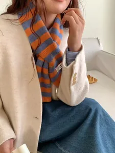 Close-up of a woman wearing an orange and blue striped wool blend pull-through scarf