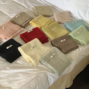 Multiple colors of solid ribbed knit scarves folded on a white bed